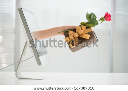 Cropped image of a human hand with a giftbox and a red rose from the computer screen