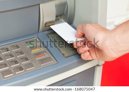 Close up image of a human hand inserting a credit card in the ATM