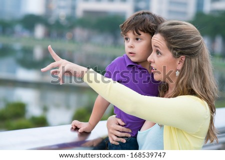 Close up image of a mother holding her son on hands and pointing at something in the street