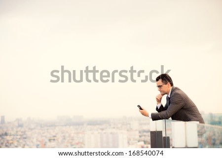 Copy-Spaced Image Of A Serious Businessman Standing On The Roof And Holding A Mobile Phone