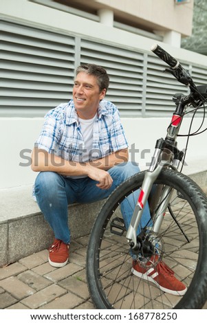Vertical image of a man resting after cycling near his bicycle on the foreground
