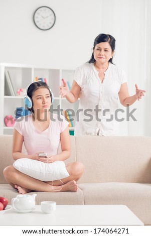Vertical image of a teenager I differently listening to the music in headphones while her mother addressing to her on the foreground