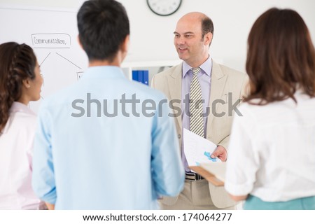Image of a smiley boss with documents in hands standing and talking with his partners after business conference on the foreground