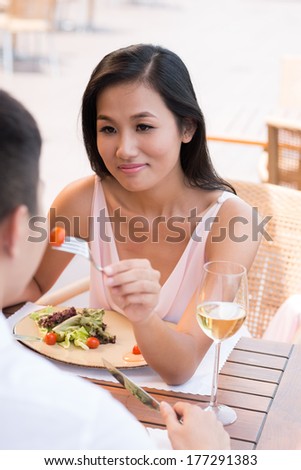 Vertical image of a young elegant woman sharing her dish with her sweetheart on the foreground