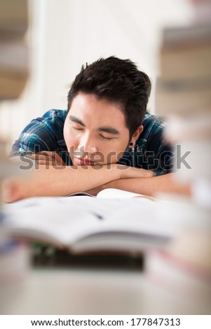 Vertical image of an exhausted student sleeping at books because of serious preparation for the exam on the foreground