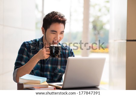 Image of a young guy drinking coffee while computing at a student cafe