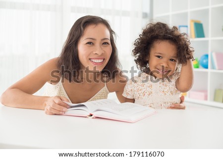 Image of a smiling mom with her little daughter with a book posing at camera