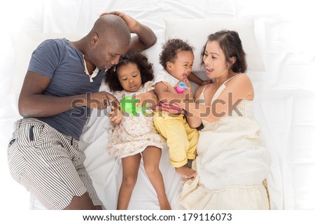 Above view of a big mixed family lying on the bed, parents playing with their little children