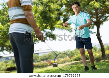 Image of a cheerful guy playing badminton with his father in the park