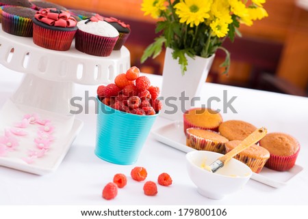 Shot of fresh raspberries on the table, delicious cakes and flowers are nearby