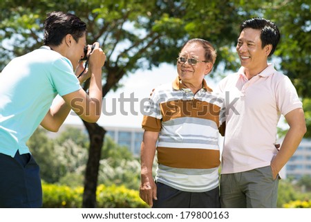Image of a guy making a photo of his father and grandfather in the park on the foreground