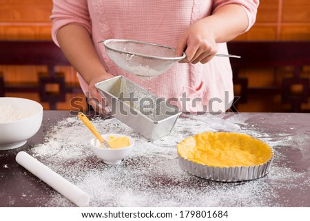 Image of a female baker sifting flour through a sieve for a baking on the foreground