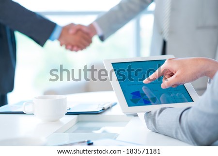 Cropped image of a business person pointing at the company activity diagram on the foreground, colleagues handshaking on the background