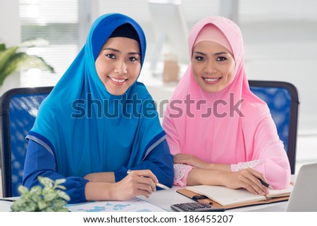Two beautiful smiling Muslim businesswoman sitting at the workplace