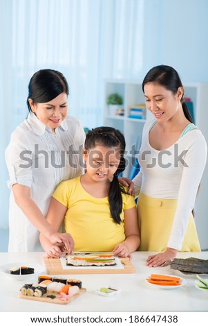 Portrait of cute little girl, her mother and grandmother cooking sushi together