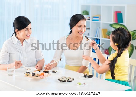 Portrait of cute little girl, her mother and grandmother eating sushi in the kitchen
