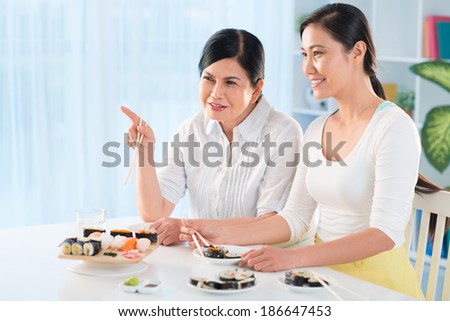 Portrait of young Asian woman and her mother talking while eating sushi in the kitchen