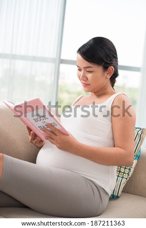 Young pregnant woman reading a book for mothers