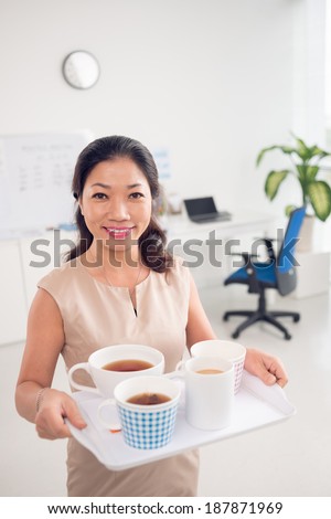 Portrait of Asian woman holding tray with cups of tea and coffee and looking at camera with smile