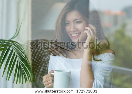 Young woman talking on the phone and drinking coffee at the window