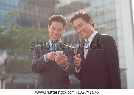 Asian businessman showing something funny on his phone to his colleague