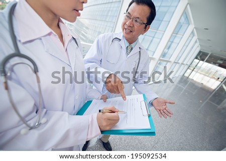 Mature Asian doctor helping intern to fill the medical paper