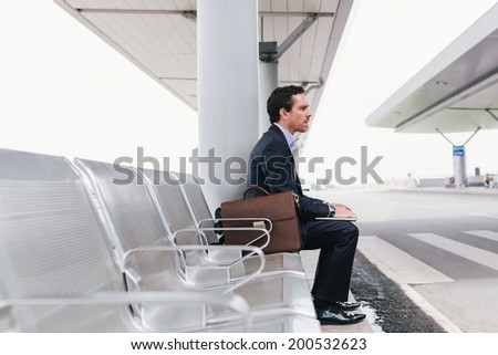 Businessman sitting on the chair at the airport bus stop and looking away side view Businessman sitting on the chair at the airport bus stop and looking away side view