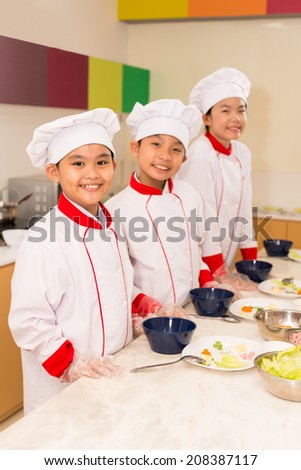 Happy Asian kids dressed as chiefs cooking in the kitchen