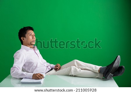 Pensive Vietnamese businessman relaxing on the chair with his feet on the table