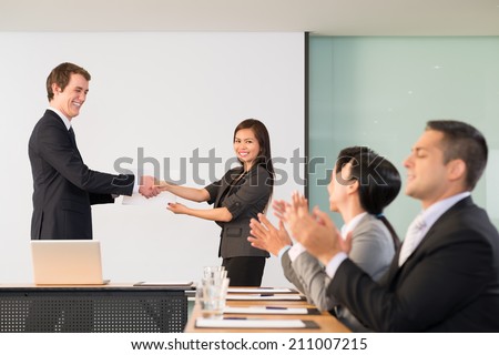 Businessman congratulating Vietnamese manager, her colleagues applauding