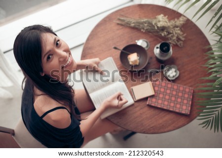 Pretty Japanese young woman looking at the camera while writing in the exercise book, view from above