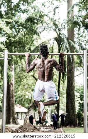 Athlete doing chin-ups in the park, rear view