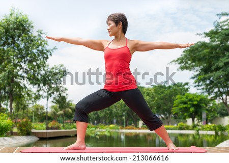 Aged Asian woman practicing warrior yoga pose outdoors