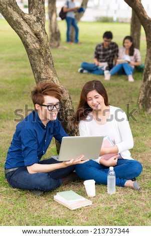 Young couple watching something on the laptop while resting on campus