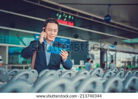 Businessman talking on the phone and reading information on his flight ticket