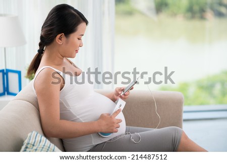 Woman with headphones on her stomach sitting on the sofa, side view