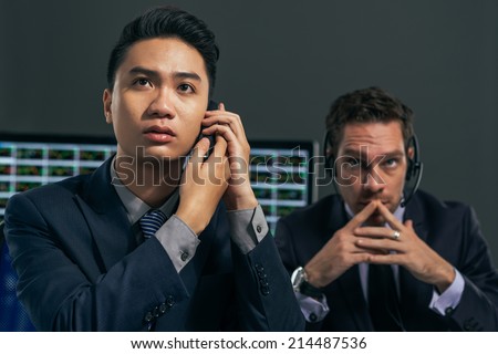 Two worried business brokers looking at the electronic stock exchange board