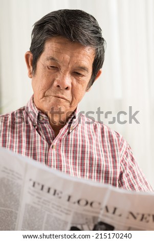 Serious Asian man reading newspaper