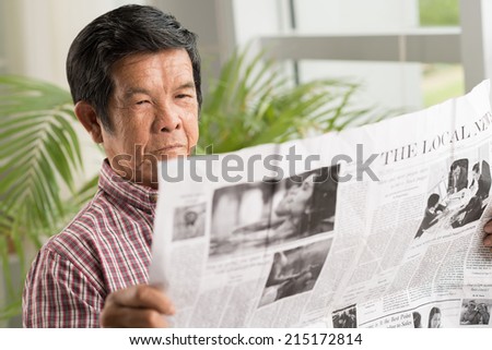 Senior Vietnamese man reading newspaper at home