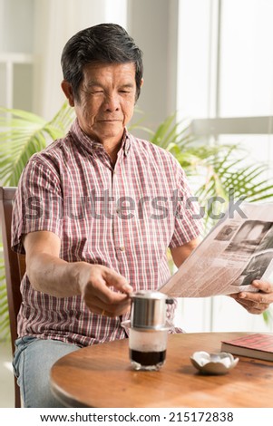 Senior Asian man drinking coffee and reading morning newspaper