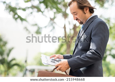Serious French businessman reading fresh newspaper outdoors, side view