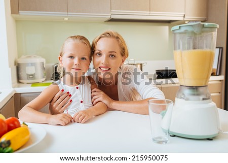 Portrait of smiling mother and daughter next to blender with healthy drink in a kitchen