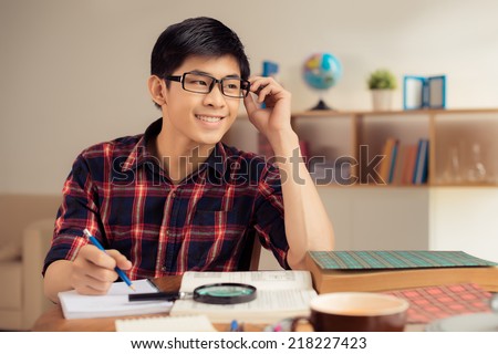 Smiling student in glasses making notes in his copybook