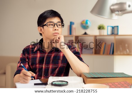 Portrait of pensive Vietnamese college student at his desk