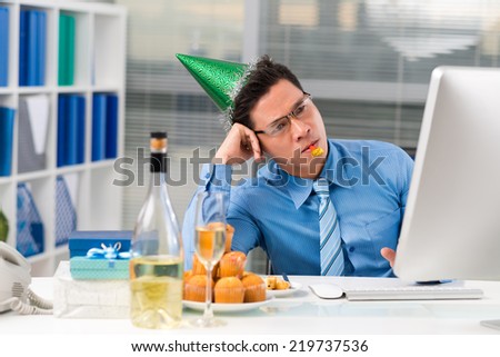 Sad Asian manager in a party hat looking at the computer screen