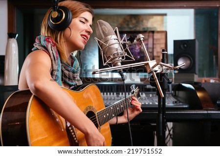 Young woman with guitar recording a song in the studio