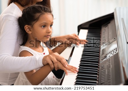 Woman helping her daughter to play the piano, body and buttons of the piano were digitally modified