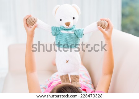 Girl playing with handmade knitted toy lying down on sofa