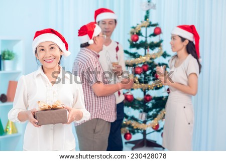 Cheerful Vietnamese woman with a gift on the background of her family celebrating Christmas