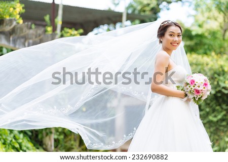 Beautiful Asian bride with her long veil fluttering in the wind